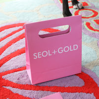 Pink 'SEOL+GOLD' bag on a colorful patterned carpet - seolgold