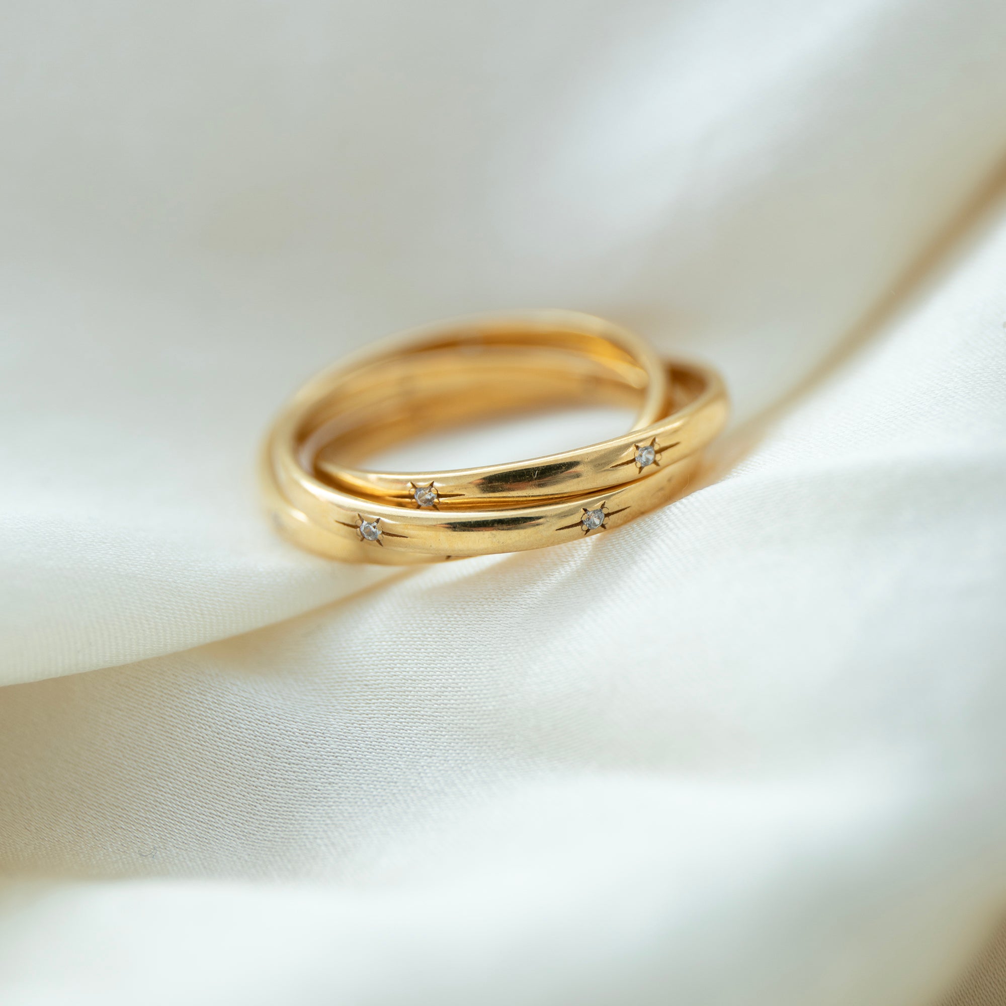Two gold rings with embedded diamonds on a white satin background - seolgold