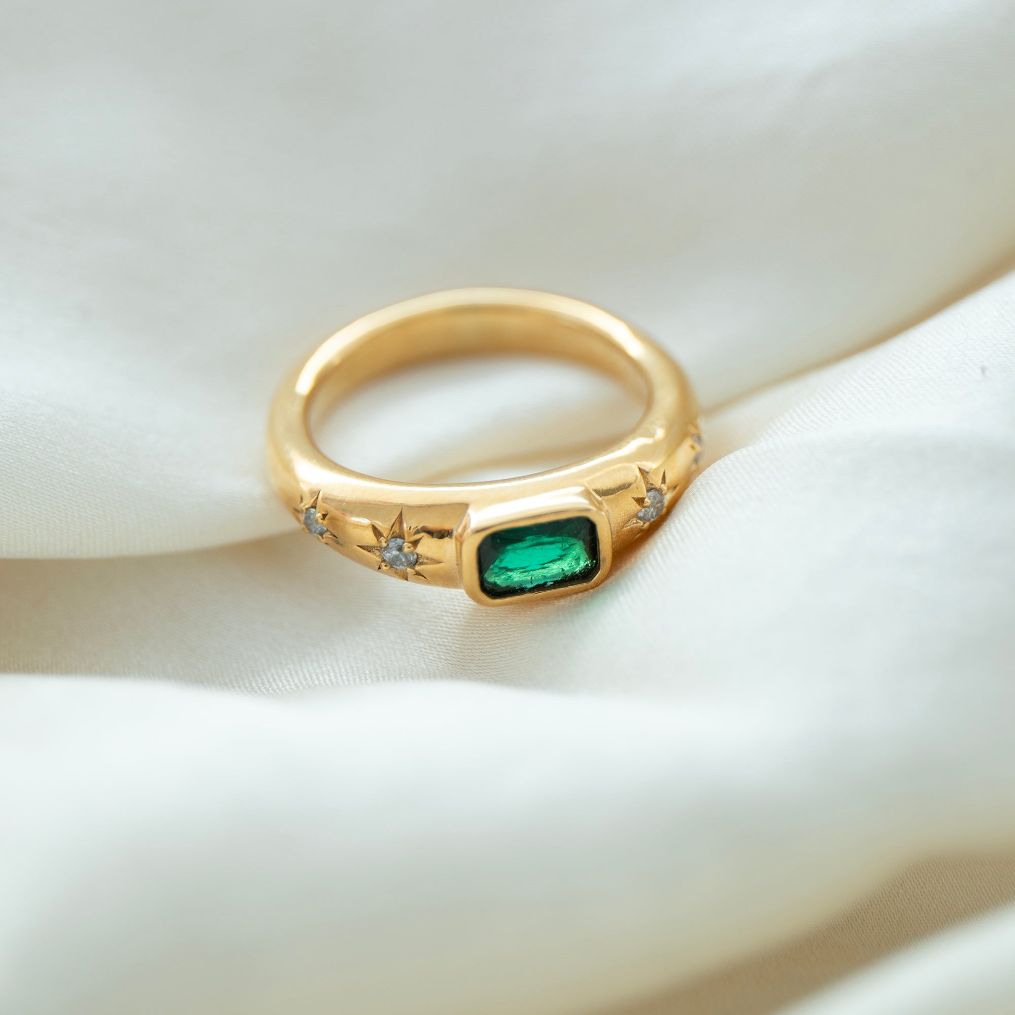 Gold ring with a green gemstone on a white fabric background - seolgold