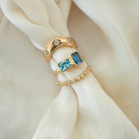 Gold rings with blue gemstones and small diamonds on a beige fabric - seolgold 