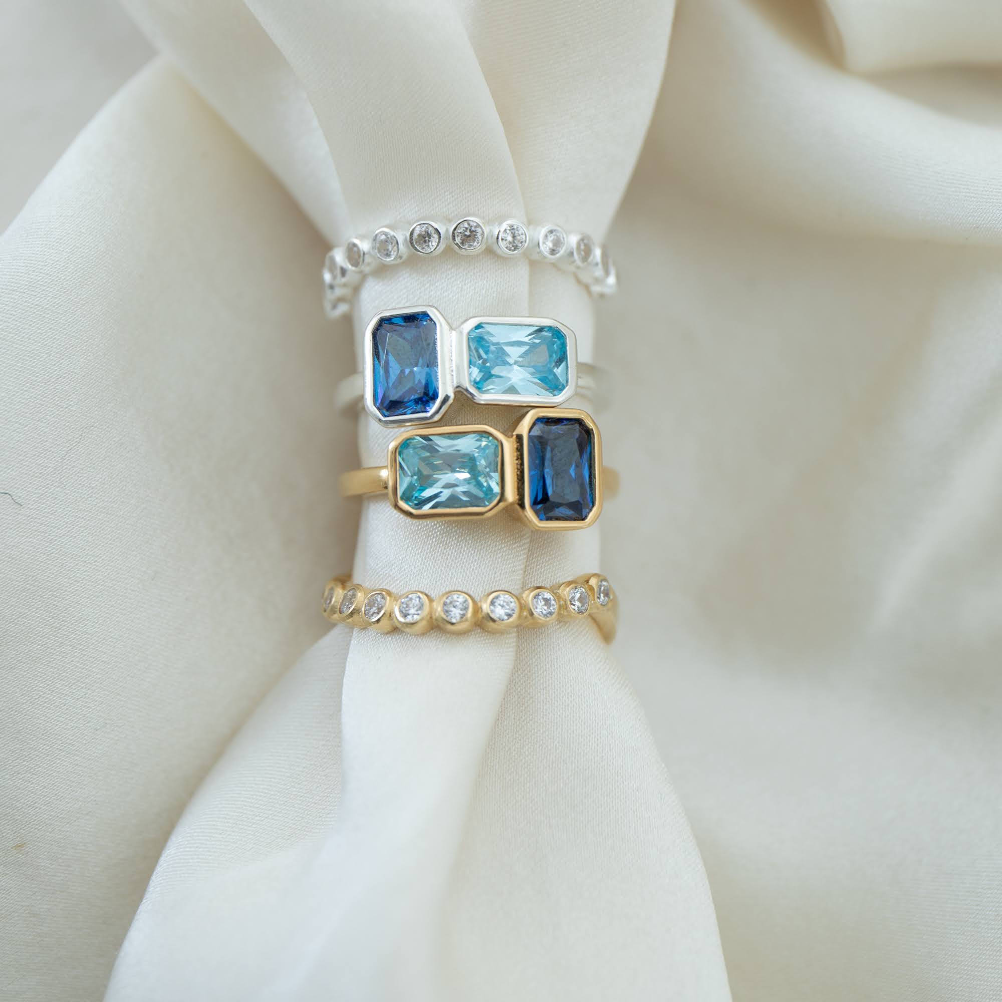 Set of rings with blue gemstones and white stones on a white fabric background - seolgold