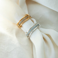 Two rings, one gold and one silver, with blue gemstones on a white fabric background - seolgold