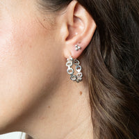Close-up of an ear wearing a silver hoop earring with a blurred background - seolgold