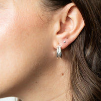 Close-up of an ear wearing a silver hoop earring with a blurred background - seolgold