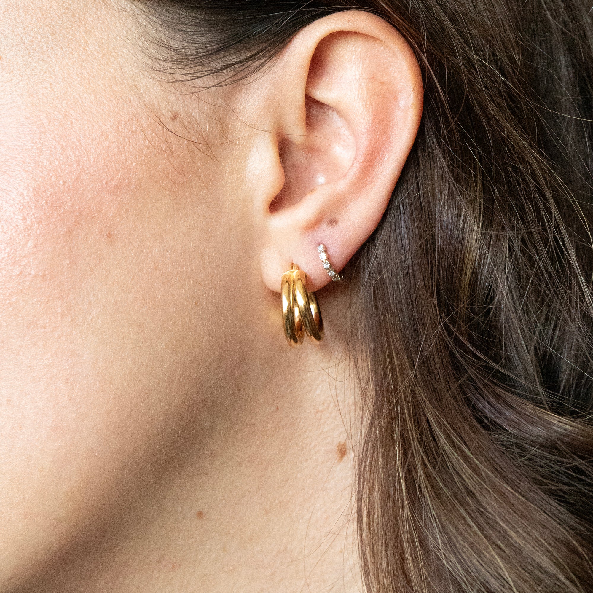 Close-up of an ear wearing gold hoop earrings with a neutral background - seolgold
