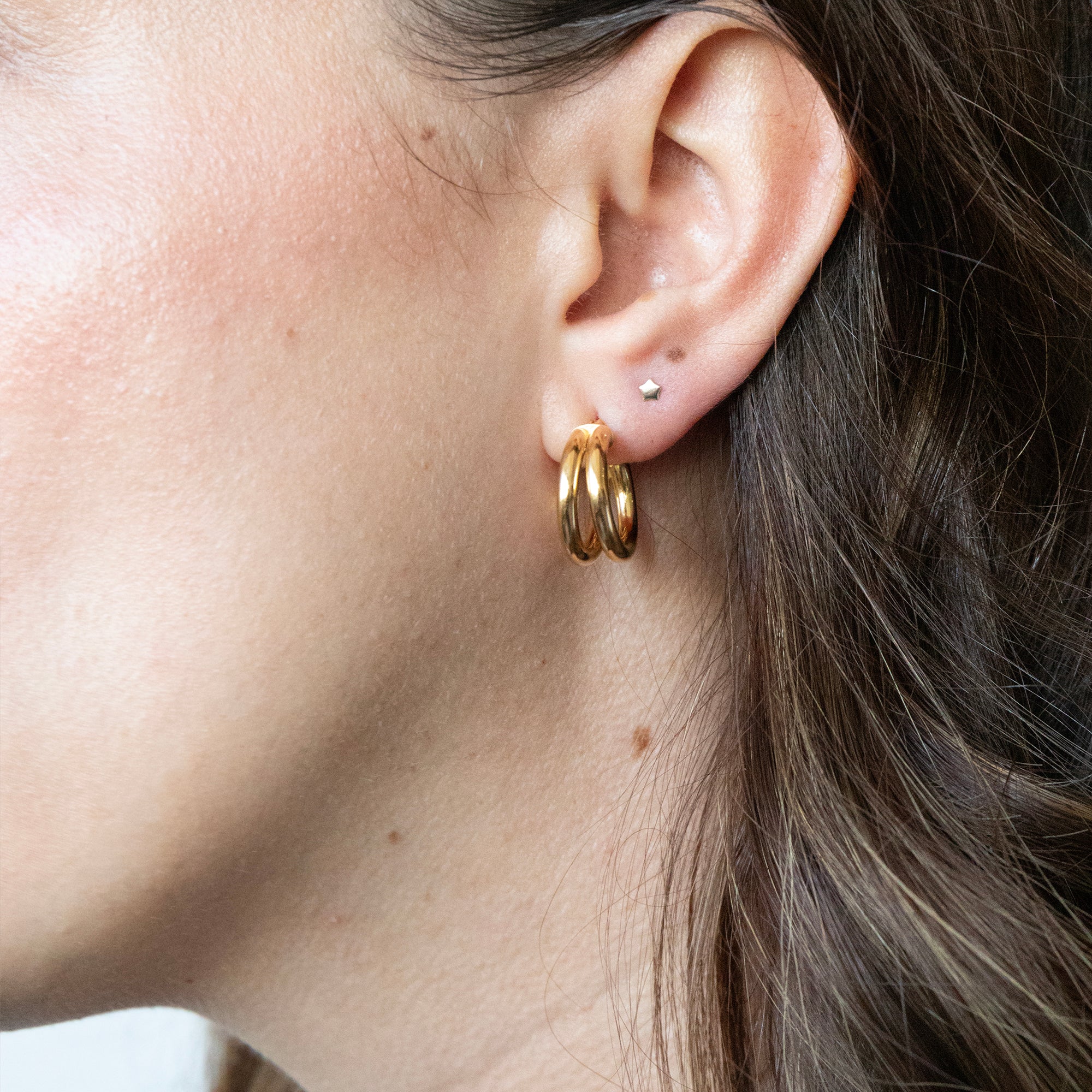 Close-up of an ear wearing gold hoop earrings with a neutral background - seolgold