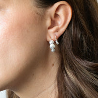 Close-up of a person wearing silver earrings with a neutral background - seolgold