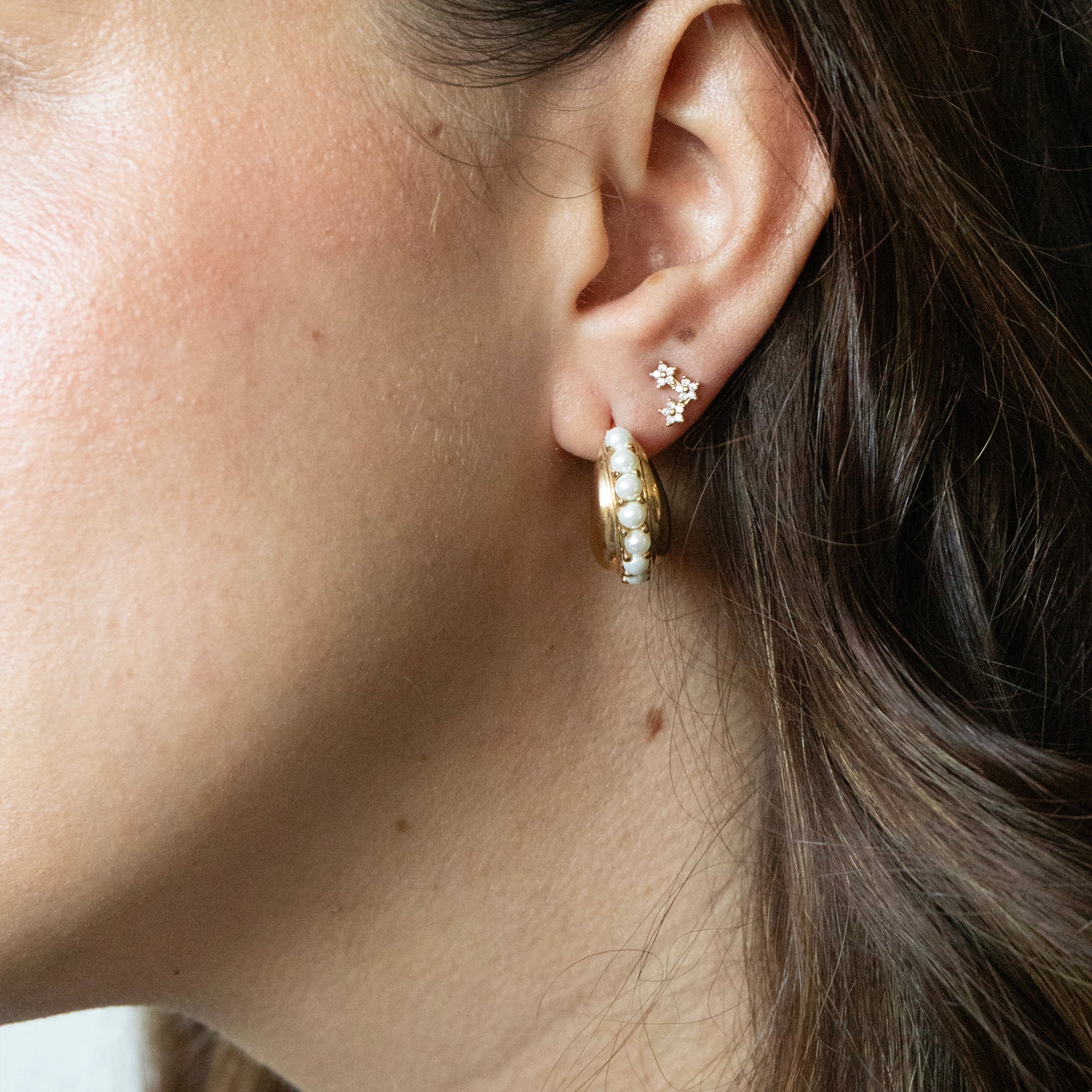 Close-up of an ear wearing gold hoop earrings with flower star-shaped studs - seolgold