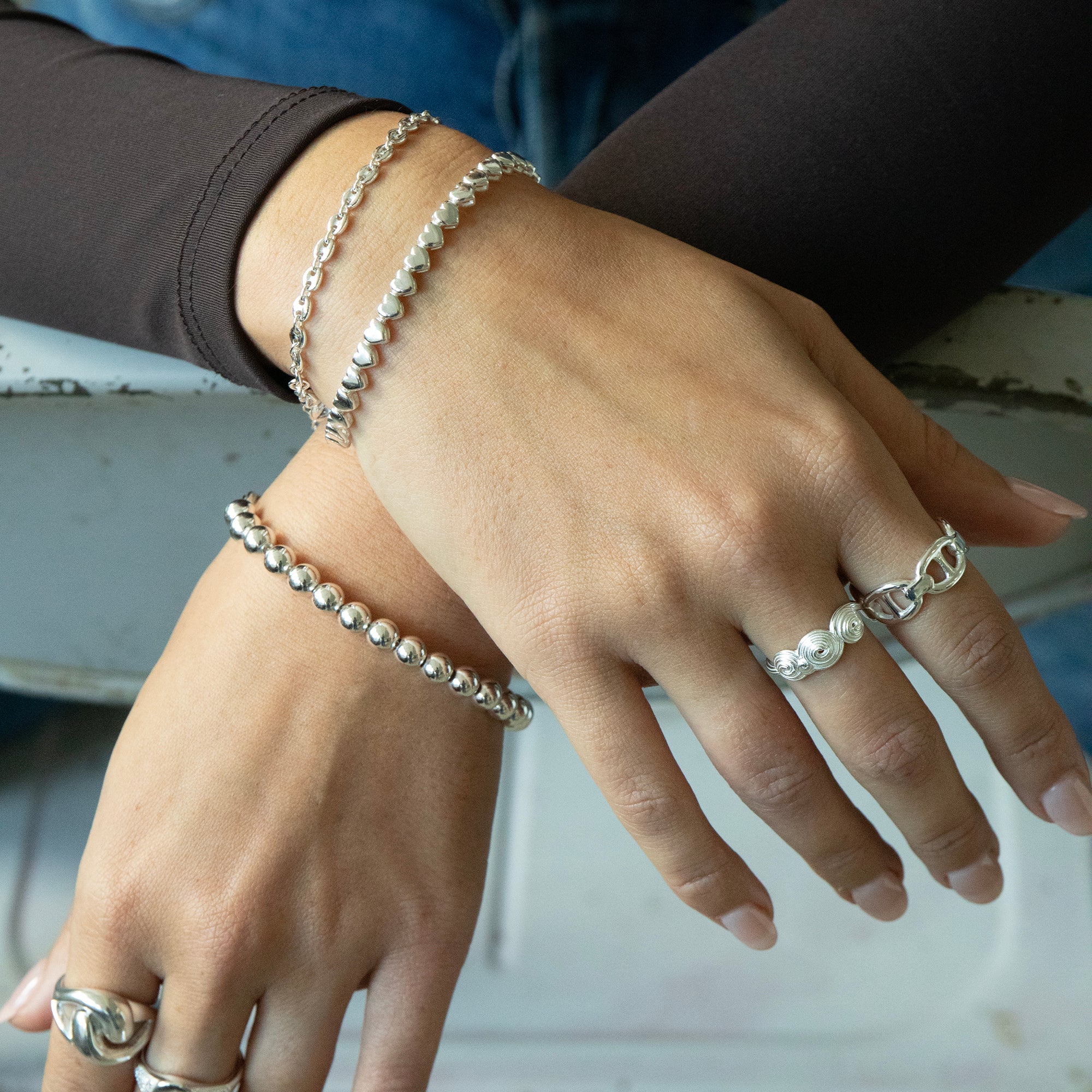 Close-up of hands wearing silver bracelets and rings on a blurred background - seolgold