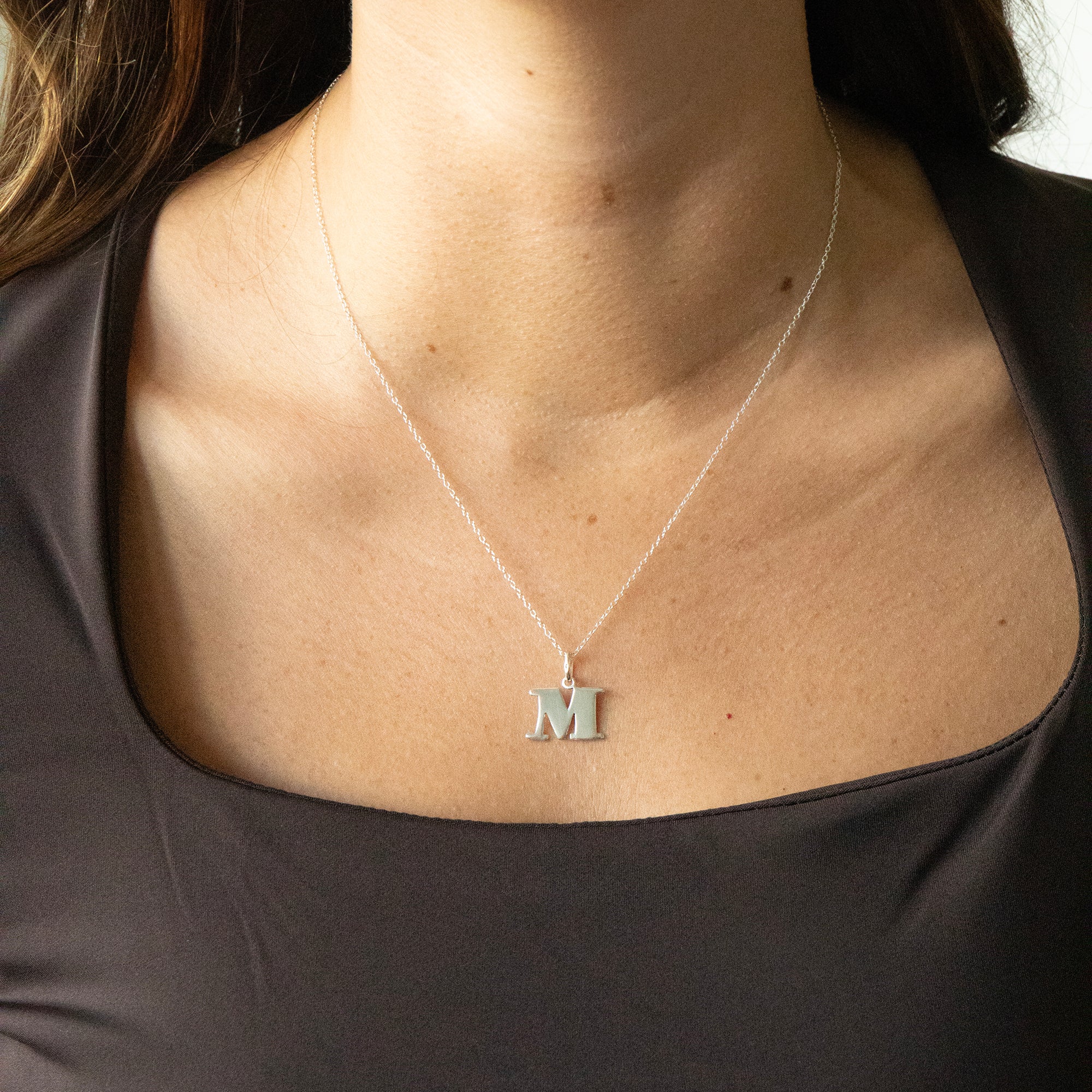 Silver necklace with a 'M' pendant on a person wearing a dark top - seolgold