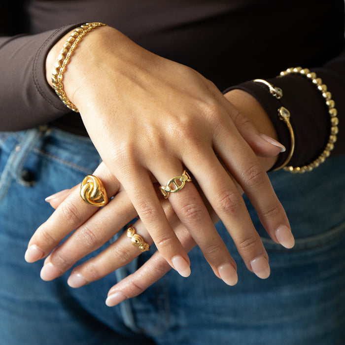Close-up of a hand wearing gold rings and bracelets against a blurred background - seolgold