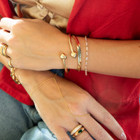 Close-up of hands wearing multiple gold bracelets and rings against a red background - seolgold