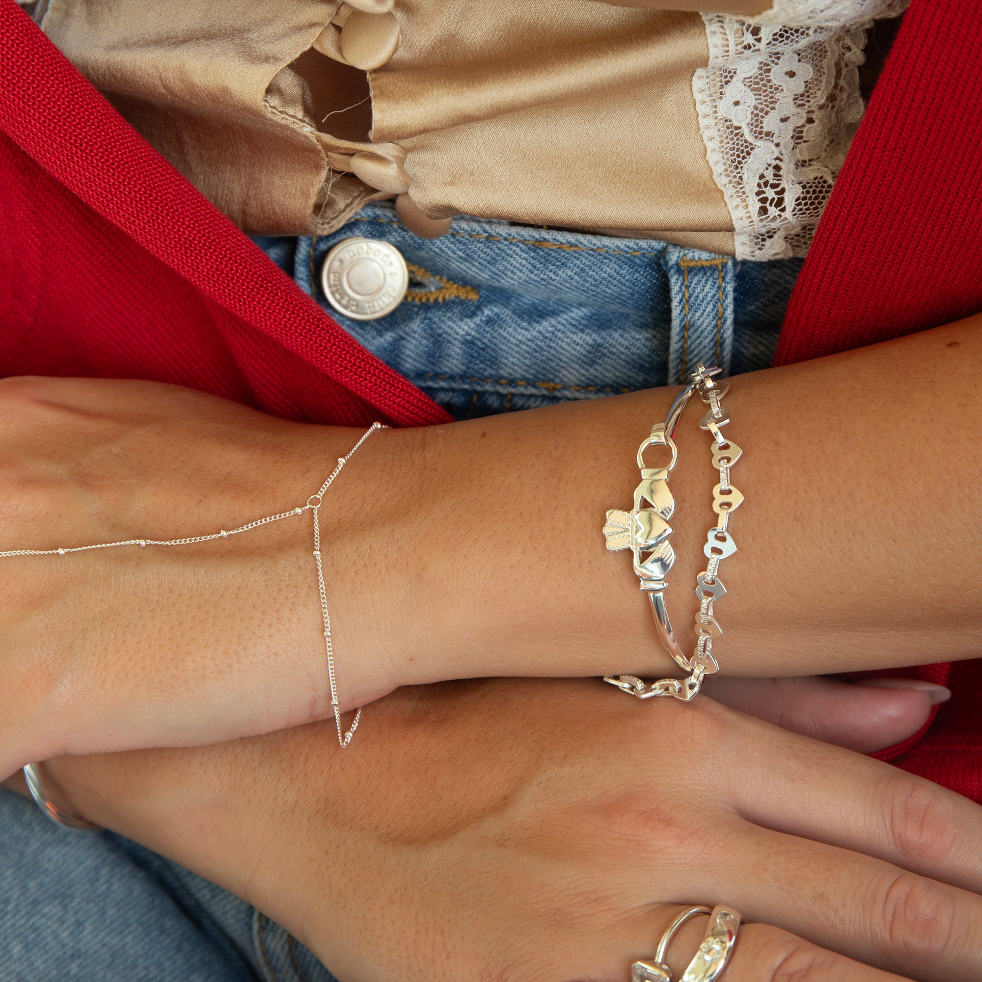 Close-up of a person's wrist wearing multiple silver bracelets on a red fabric background - seolgold
