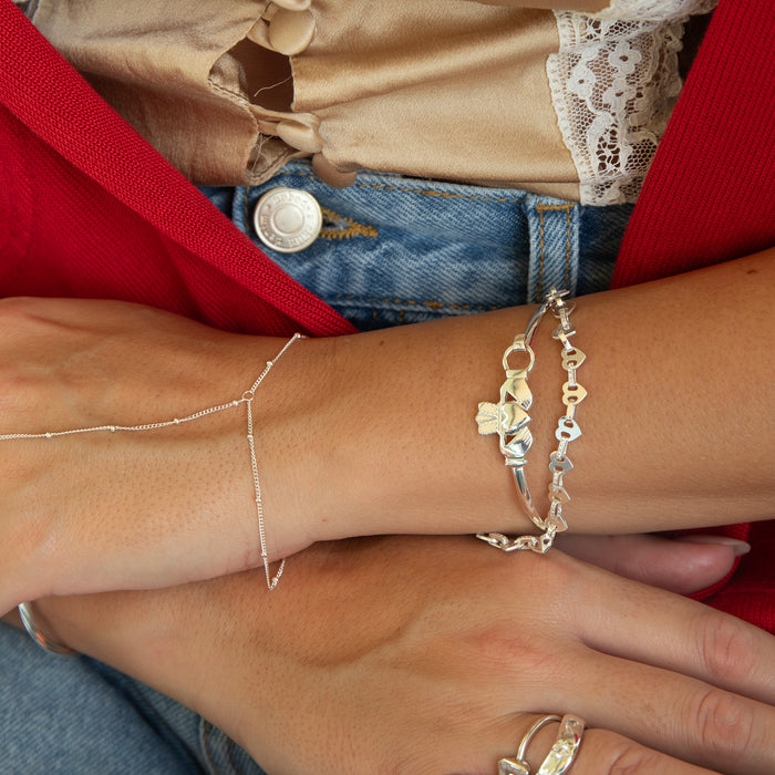 Close-up of a person's wrist wearing multiple silver bracelets on a red fabric background - seolgold