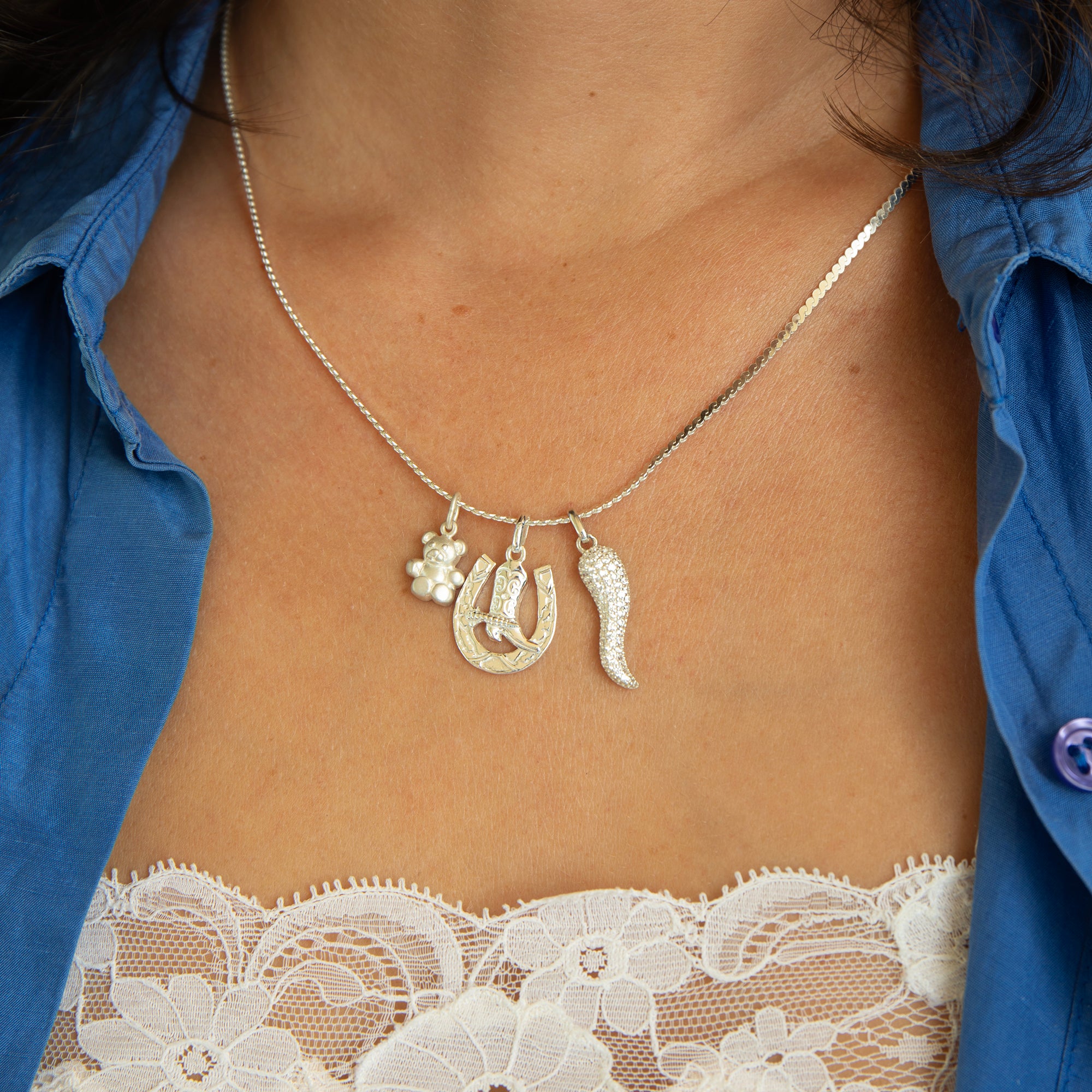 Necklace with horse shoe and boot charms worn by a person in a blue shirt and lace top - seolgold