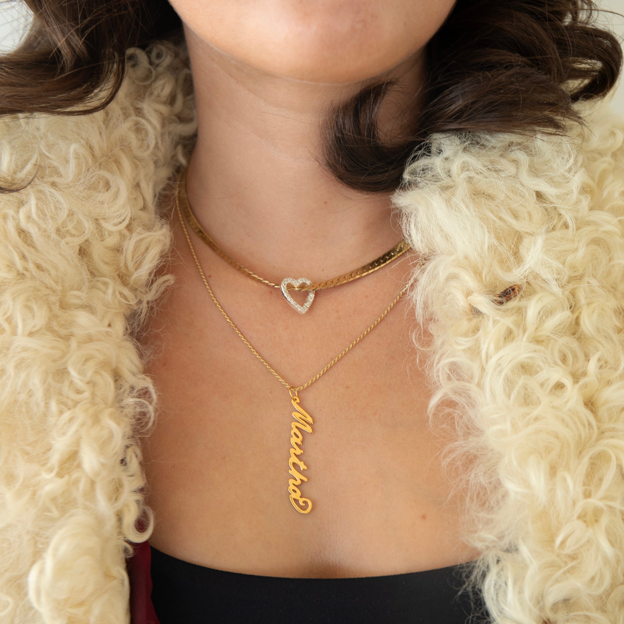 Person wearing gold necklaces with a heart and name pendant, against a textured beige background - 18ct Gold Vermeil Vertical Script Custom Name Plate - seolgold
