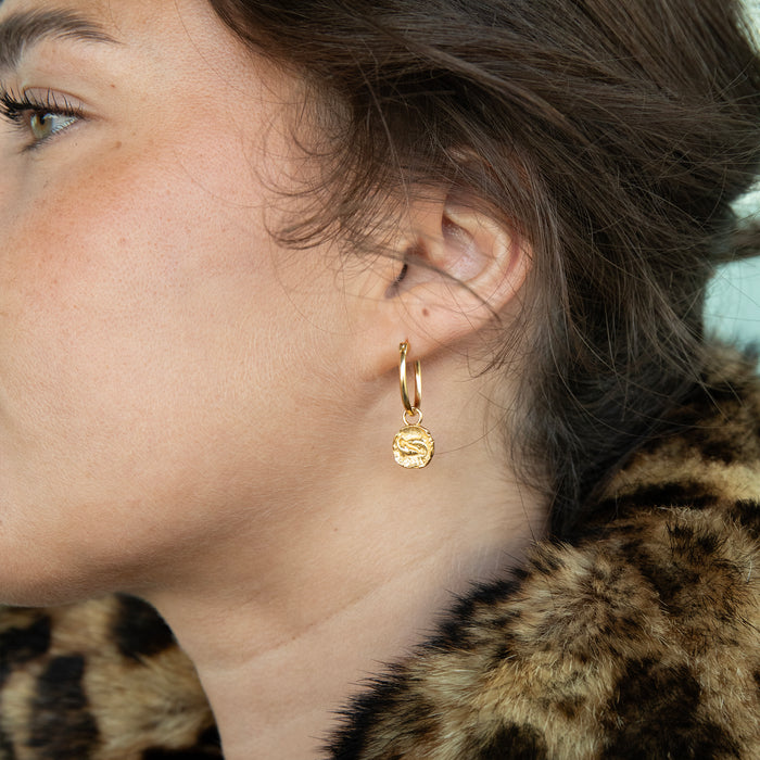 Close-up of a person wearing a gold hoop earring with a leopard print fur garment - seolgold
