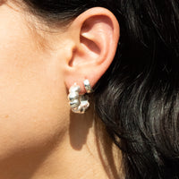 Close-up of an ear wearing silver hoop earrings with a blurred background - seolgold