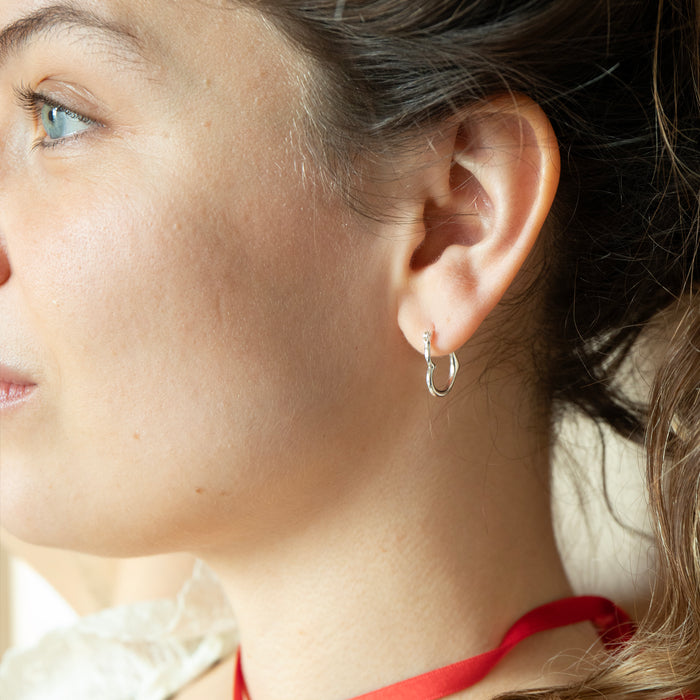 Close-up of a person wearing a small hoop earring with a neutral background - seolgold