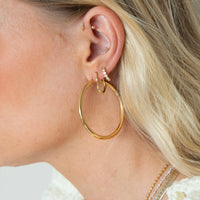 Close-up of an ear wearing gold hoop earrings with additional jewelry - seolgold