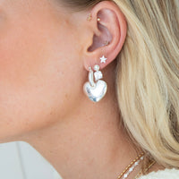 Close-up of an ear wearing silver heart-shaped earrings with a star detail - seolgold