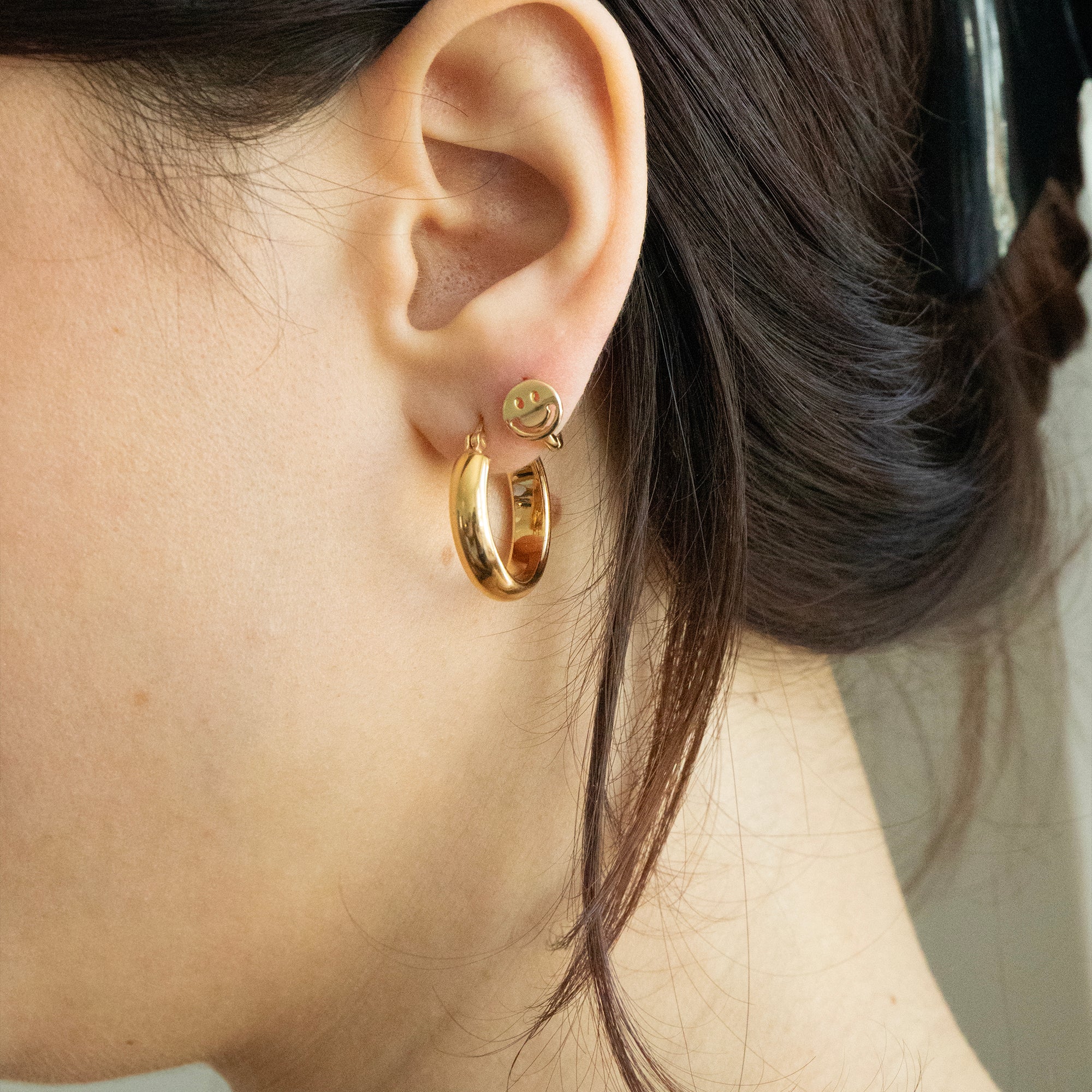 Close-up of an ear wearing gold hoop earrings with a blurred background - seolgold