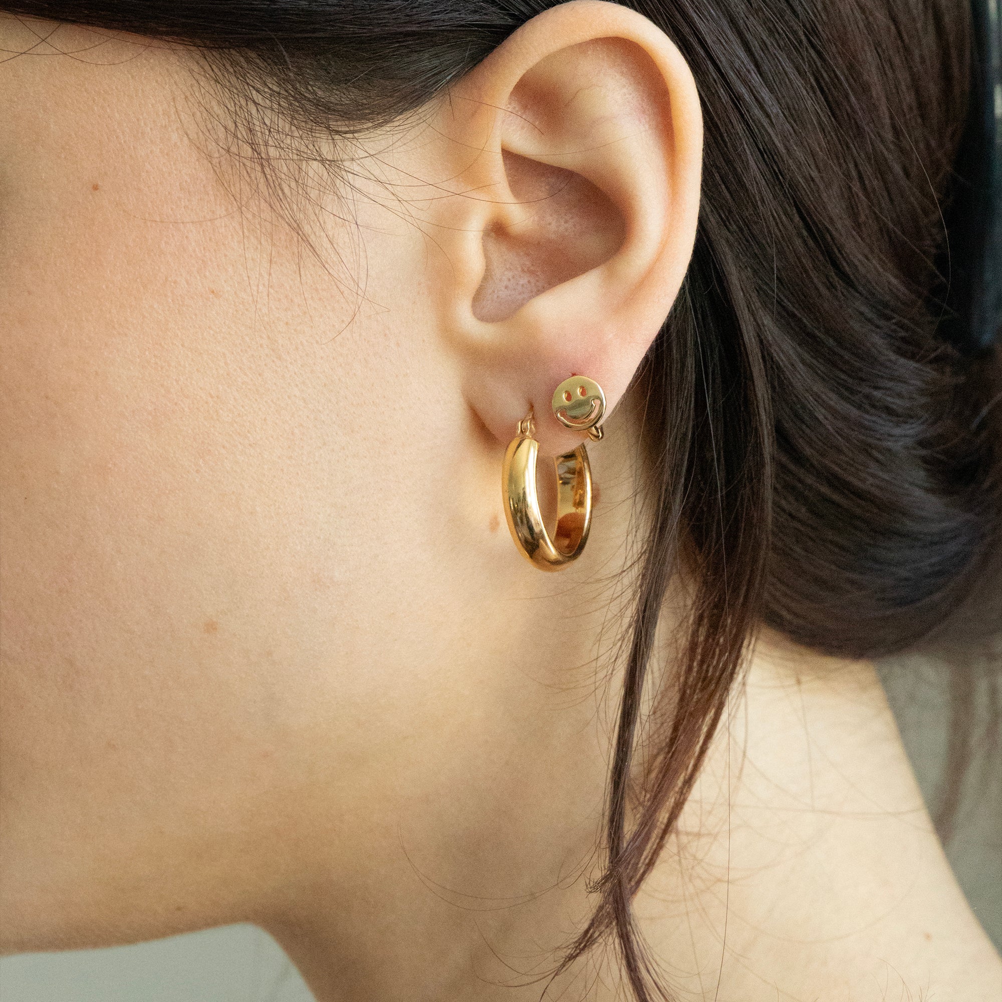 Close-up of an ear wearing gold hoop earrings with a neutral background - seolgold