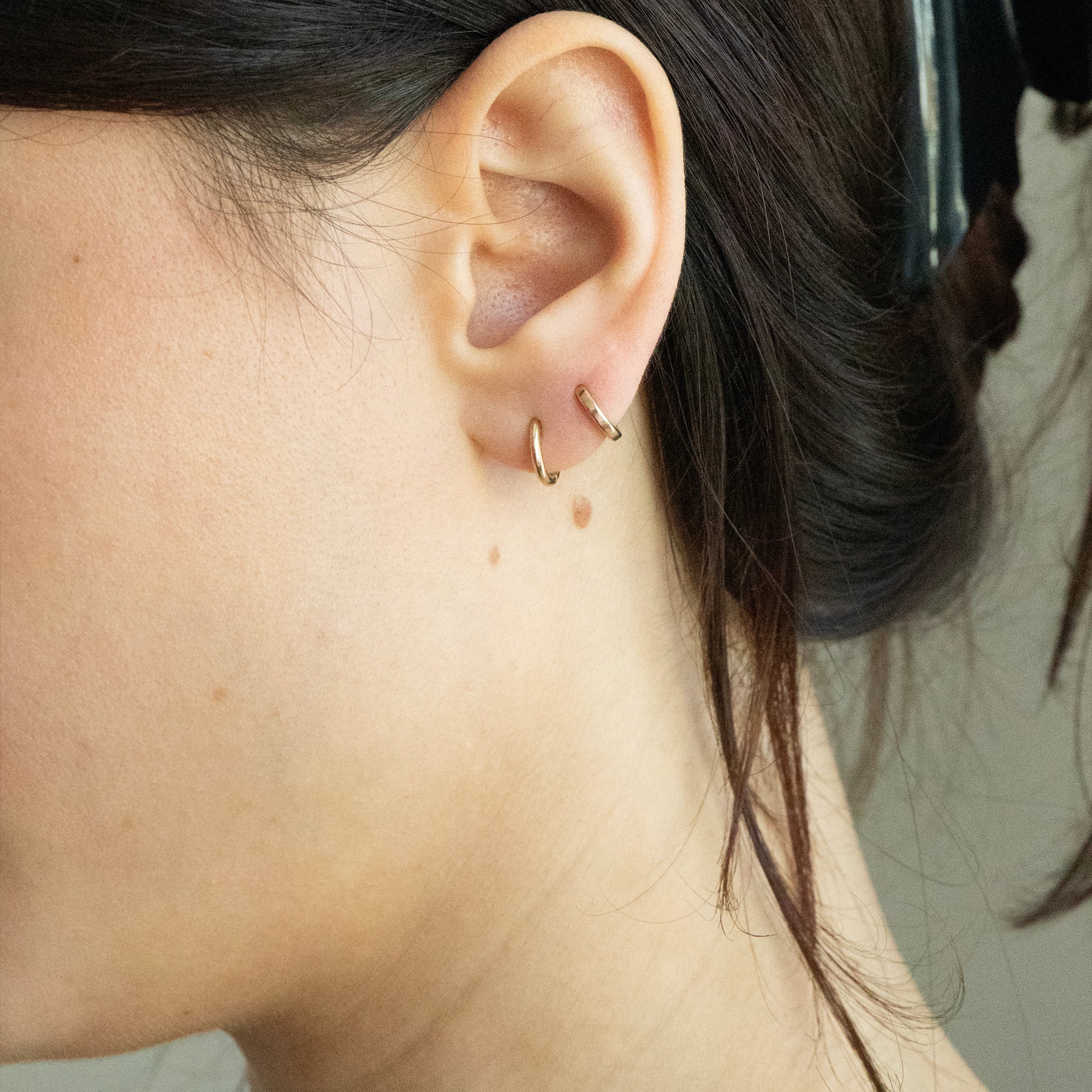 Close-up of an ear with gold hoop earrings against a neutral background - seolgold