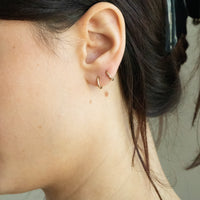 Close-up of an ear with gold hoop earrings against a neutral background - seolgold