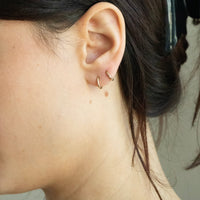 Close-up of an ear with gold hoop earrings against a neutral background - seolgold