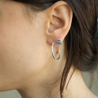 Close-up of an ear wearing a silver hoop earring with a small round charm - seolgold