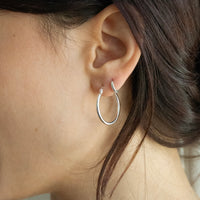Silver hoop earrings worn by a person with dark hair - seolgold