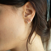 Close-up of an ear wearing a silver hoop earring with hair partially covering the face - seolgold