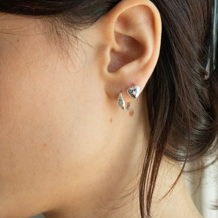 Close-up of an ear wearing a silver earring with a heart detail - seolgold