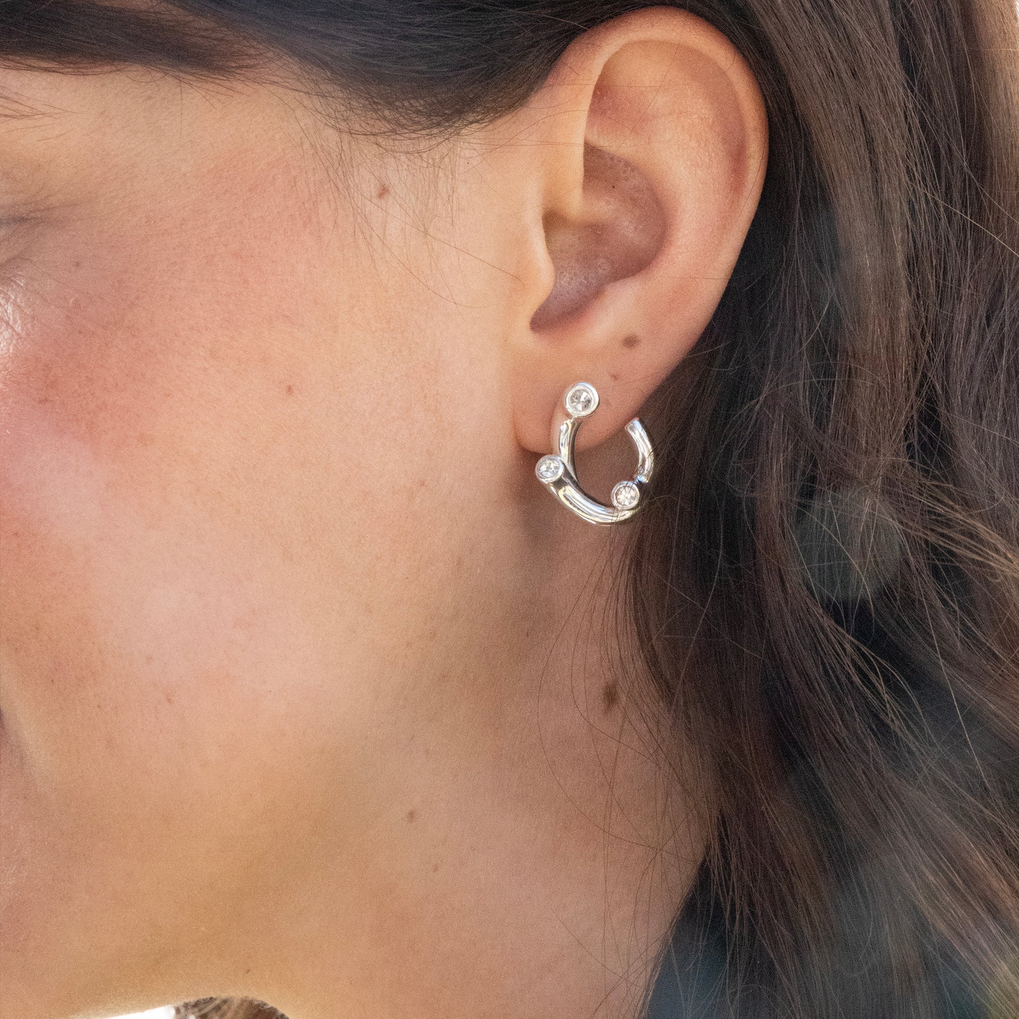 Close-up of an ear wearing a silver hoop earring with small stones - seolgold