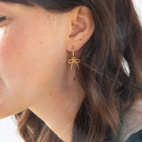 Close-up of a person wearing a gold bow-shaped earring - seolgold