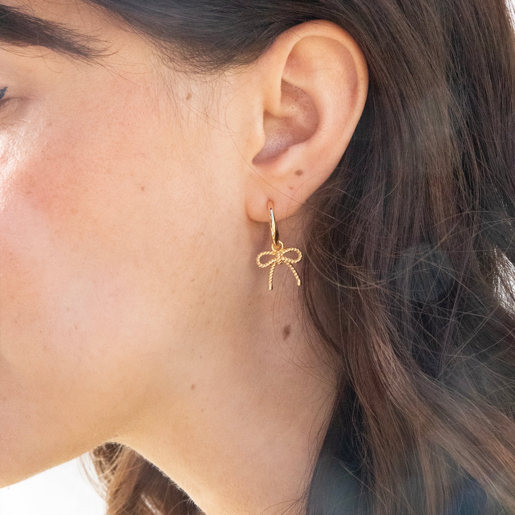 Gold bow-shaped earring worn by a person with dark hair - seolgold