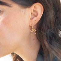 Gold bow-shaped earring worn by a person with dark hair - seolgold