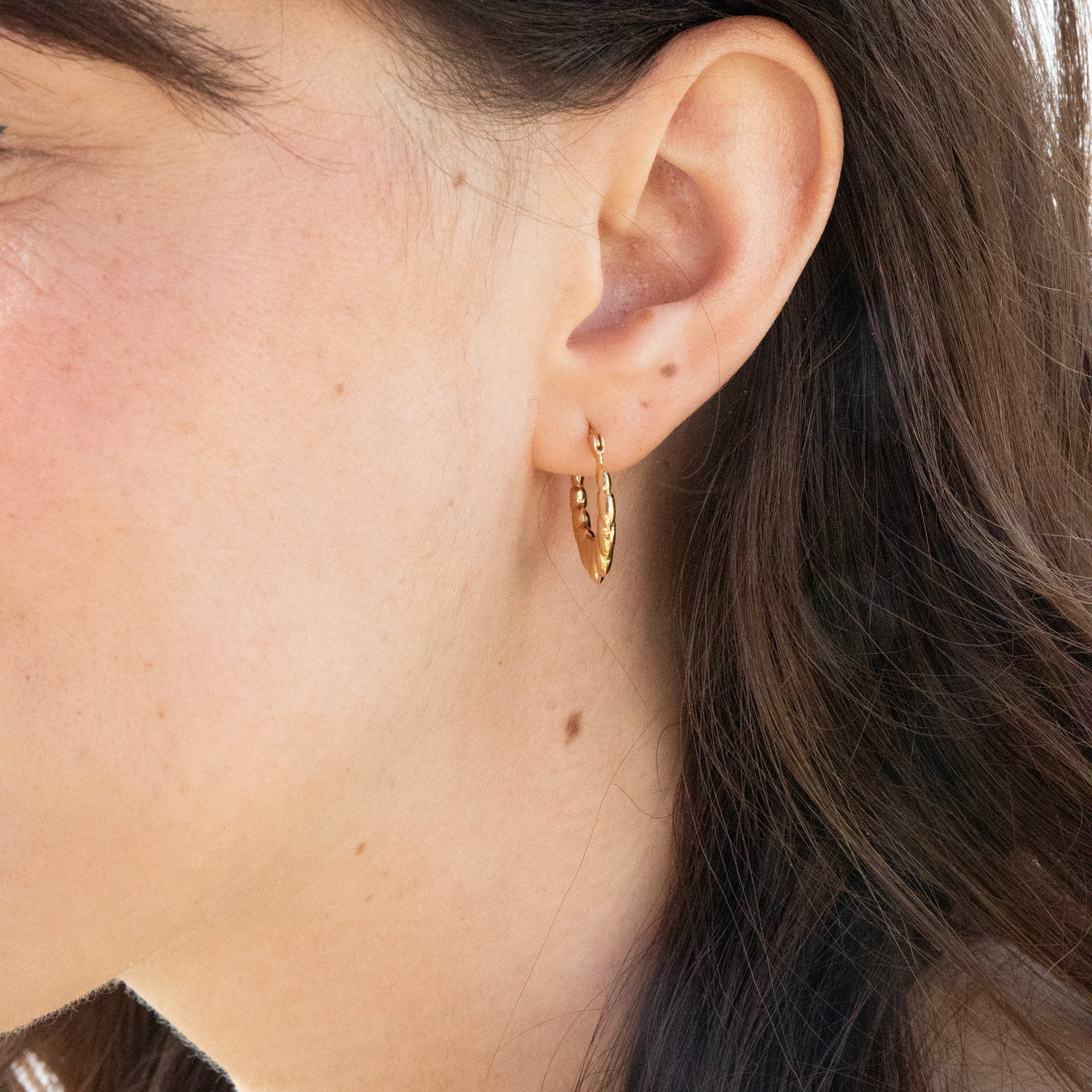 Close-up of an ear wearing a gold hoop earring with hair partially covering the face - seolgold