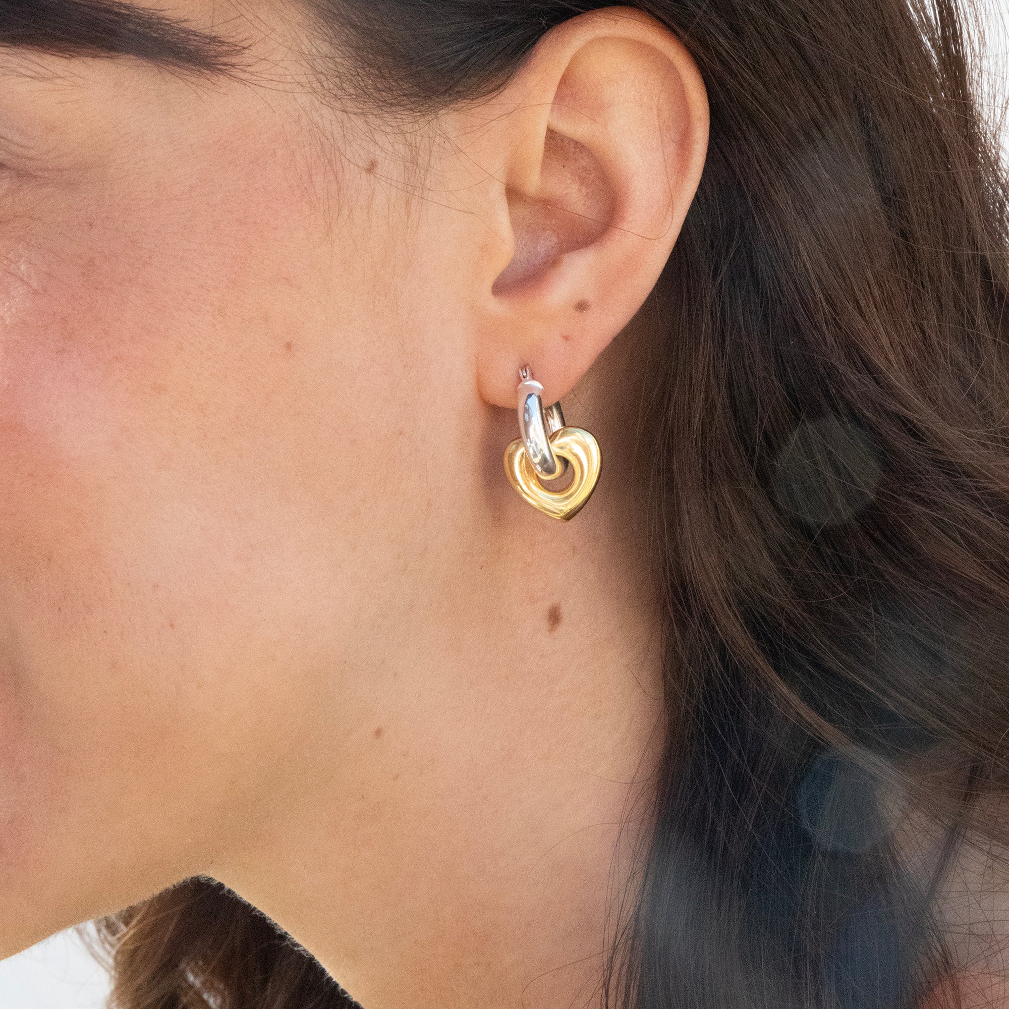 Close-up of a person wearing a gold heart-shaped earring - seolgold