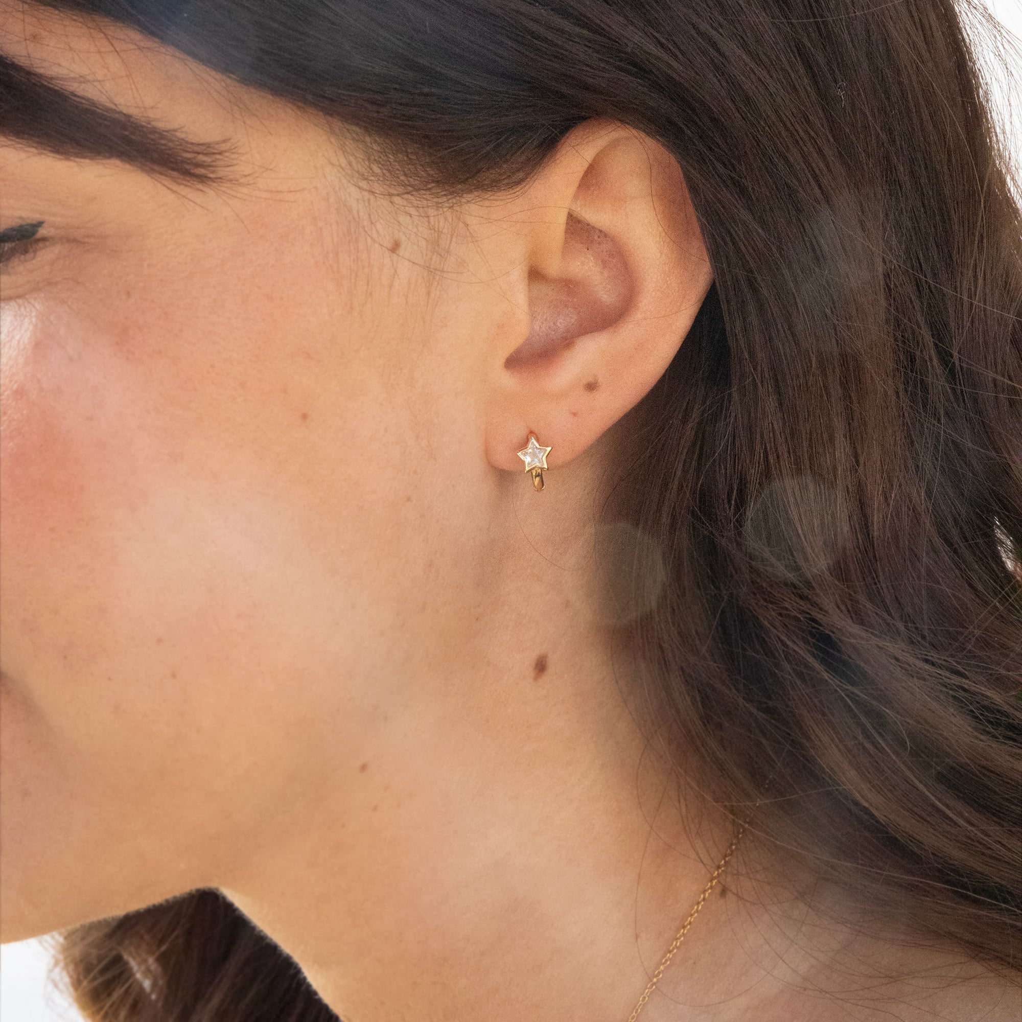 Close-up of a person wearing a tiny 
 gold star-shaped hoop earring - seolgold
