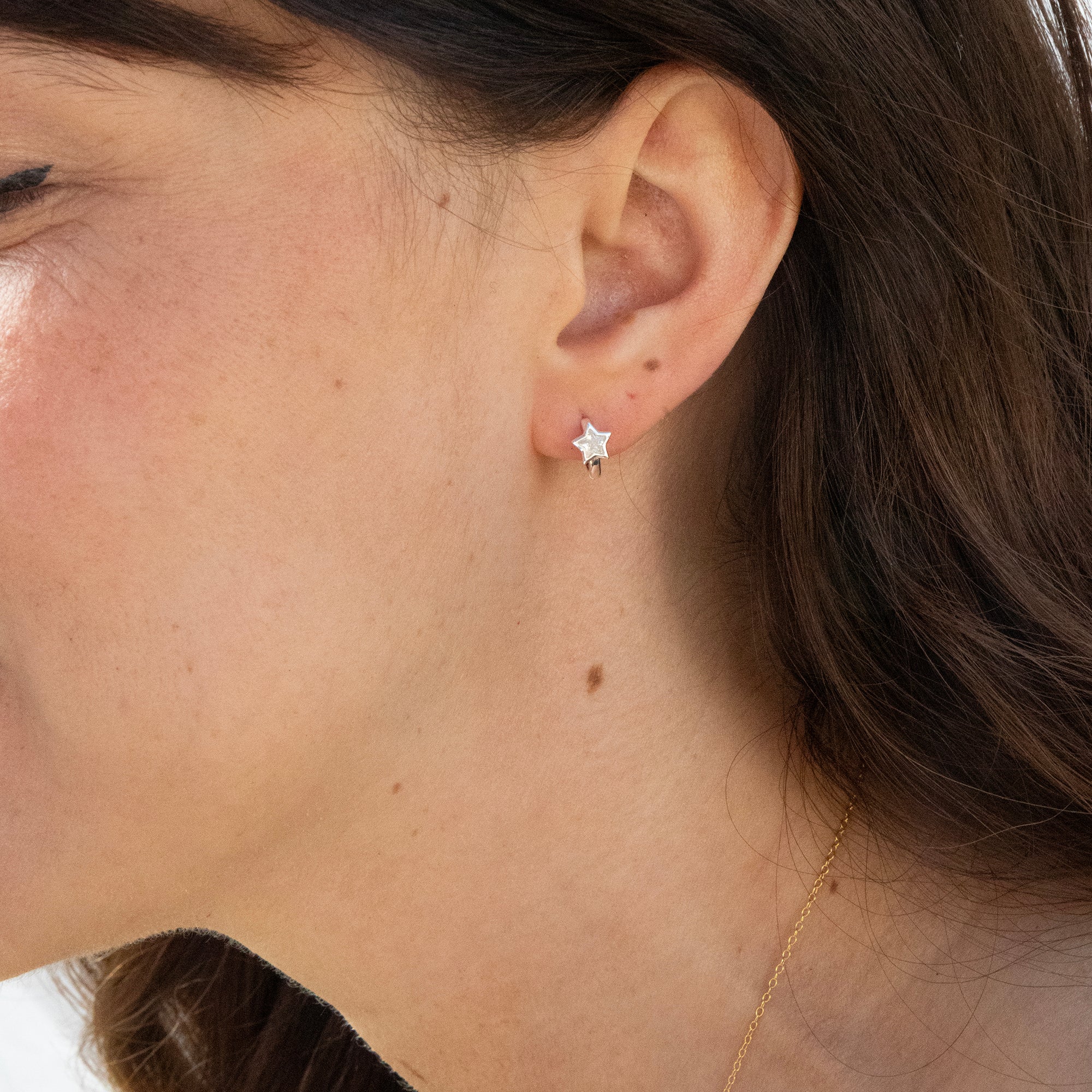 Close-up of an ear wearing a tiny star-shaped hoop earring with a blurred background - seolgold