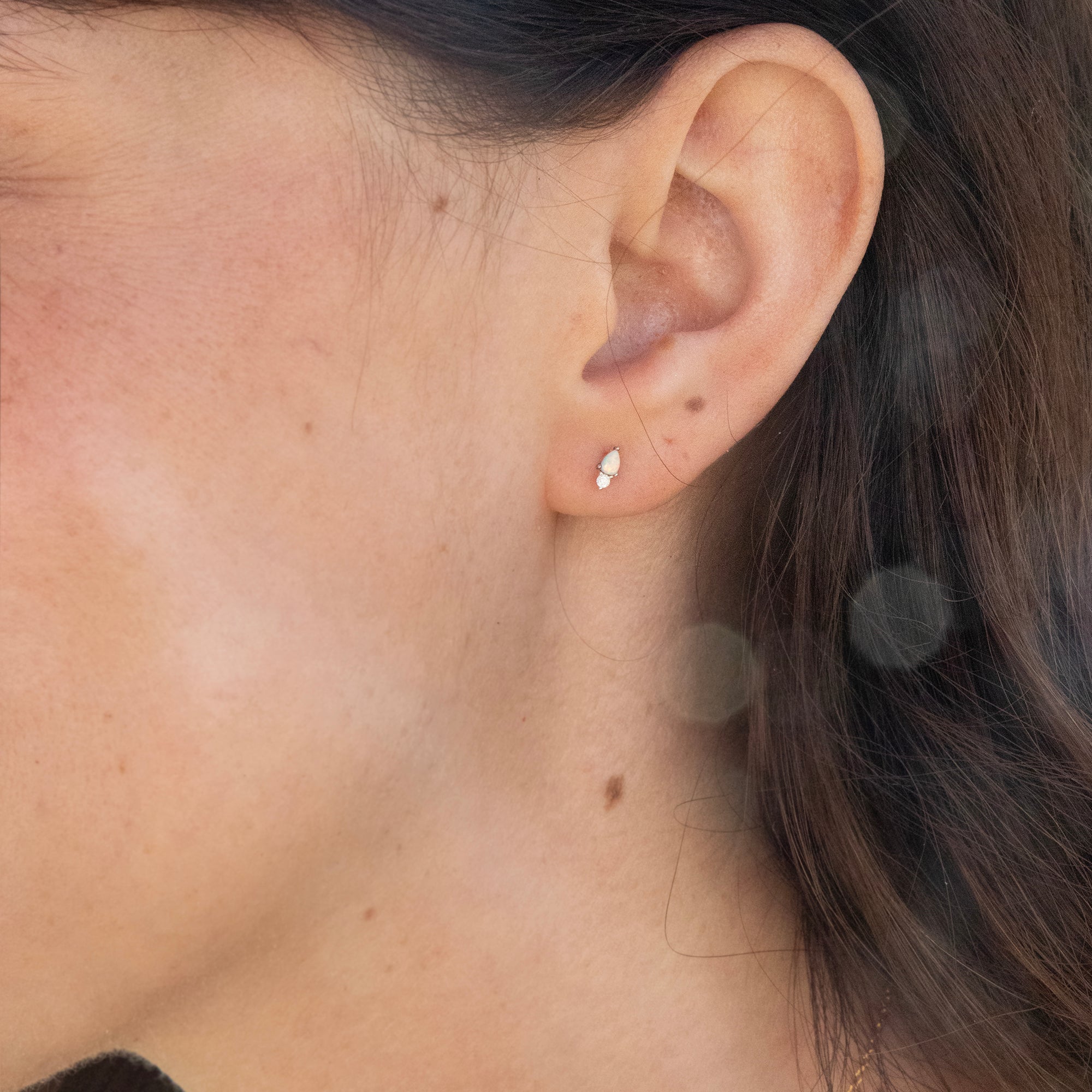 Close-up of an ear wearing a small earring with blurred hair and skin in the background - seolgold