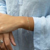 Close-up of a wrist wearing a bracelet with a green gemstone, against a light blue shirt background - seolgold