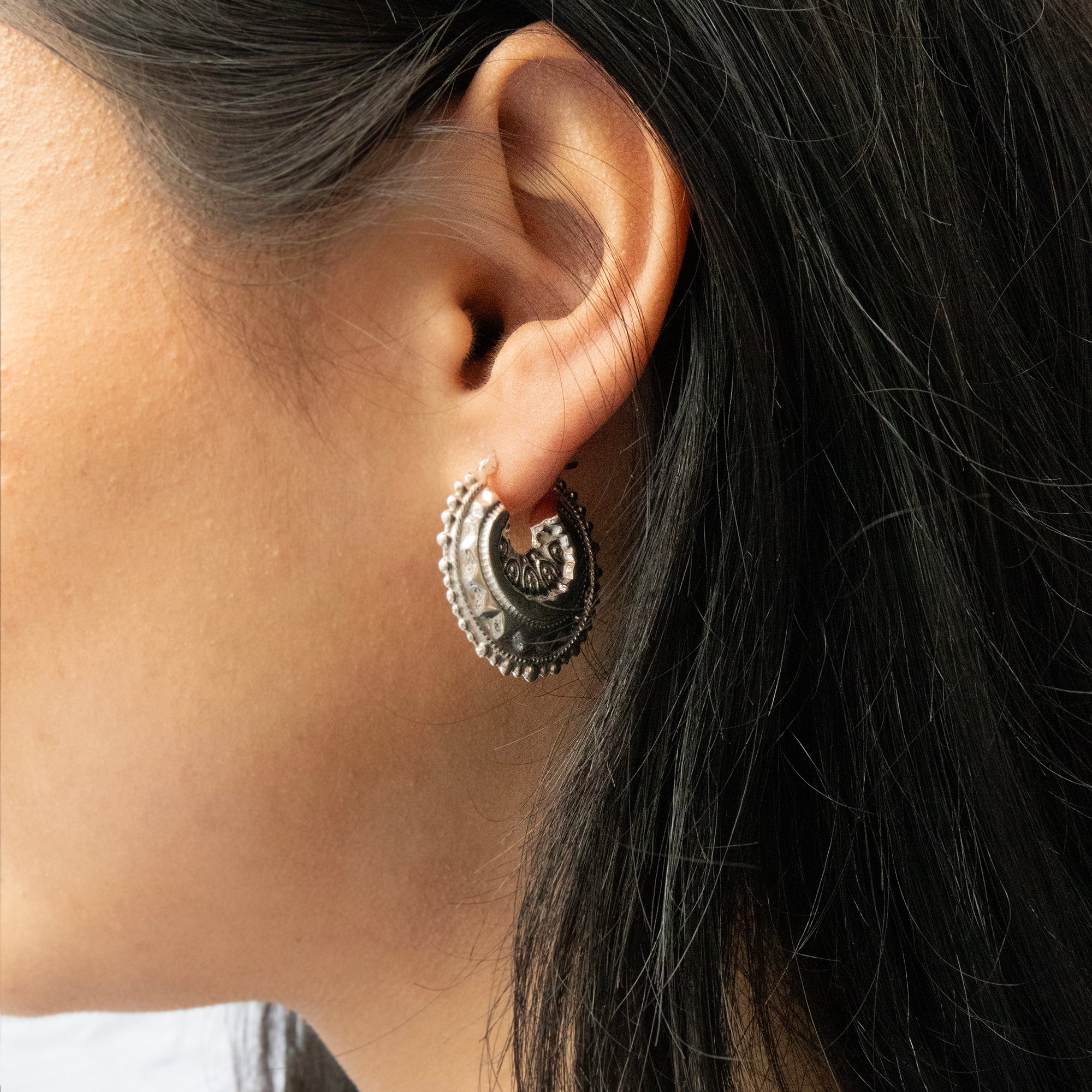 Close-up of an ear wearing a decorative hoop earring with dark hair - seolgold