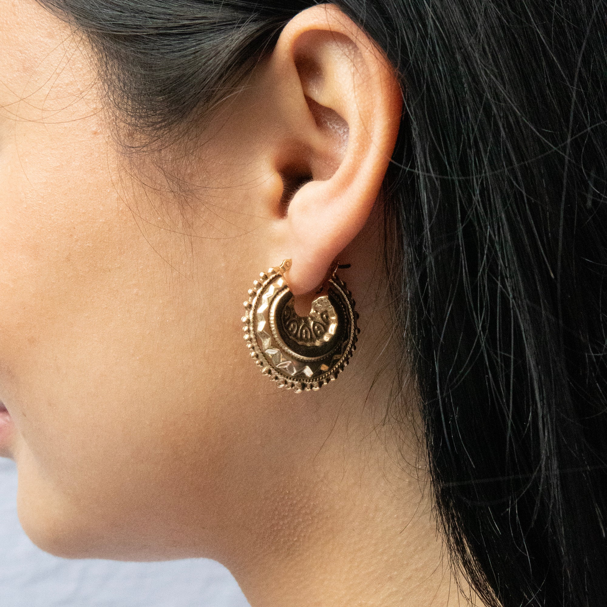 Close-up of a person wearing a gold hoop earring with intricate designs - seolgold