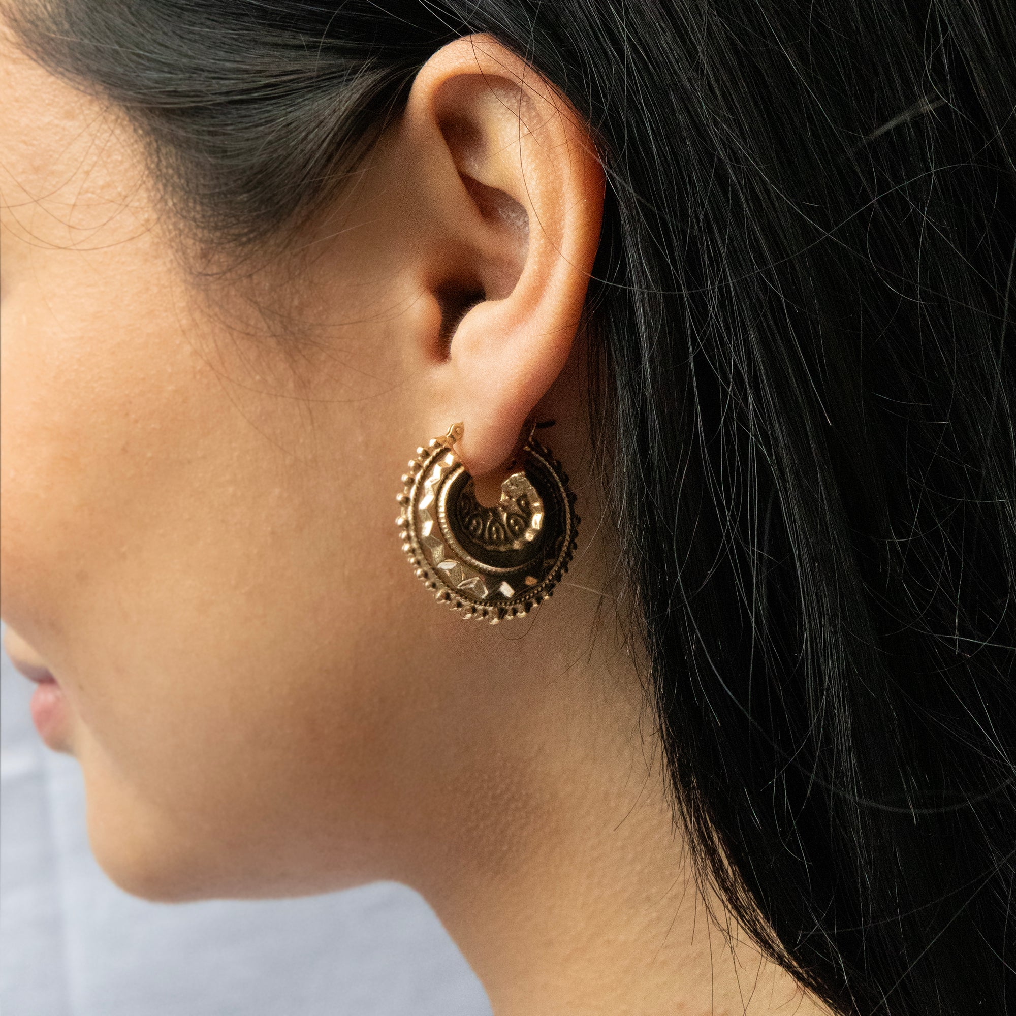 Close-up of a person wearing a gold hoop earring with intricate designs - seolgold