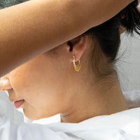 Close-up of a person wearing a gold hoop earring with a blurred background - Mixed Metal Shaker Hoop Earrings - seolgold