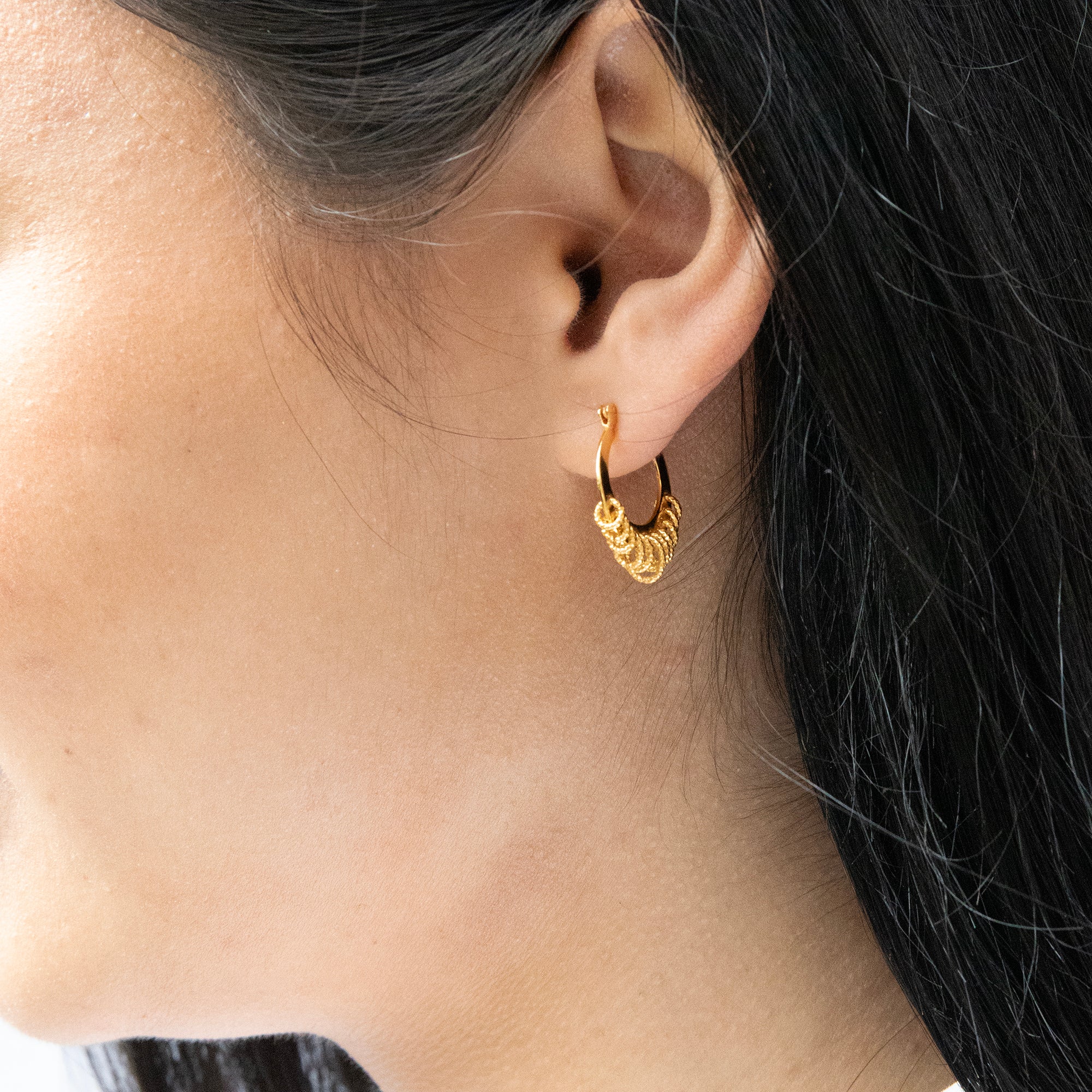 Close-up of a person wearing a gold hoop earring with a blurred background - seolgold