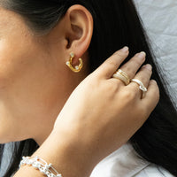 Close-up of a person wearing gold hoop earrings, rings, and bracelets - seolgold